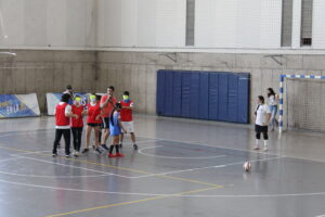 Profesor enseña cómo se realiza la dinámica de penales en partido de fútbol adaptado. Estudiantes en cancha participan con él.