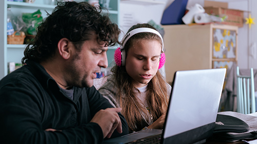 Hombre apoya a una chica con discapacidad visual frente a un computador.