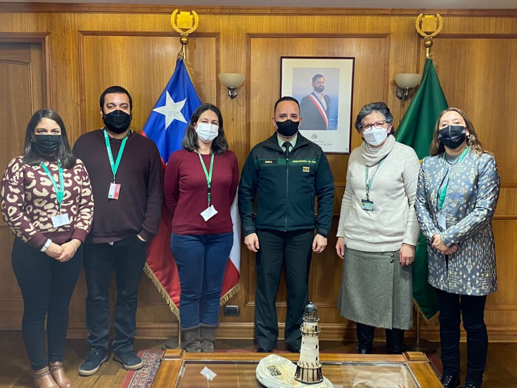 Autoridades, funcionarios y funcionaras de Gendarmería de Chile y de la Dirección de Inclusión posando frente a la cámara. De fondo, se ve la bandera de Chile en un mástil y la fotografía del Presidente Gabriel Boric