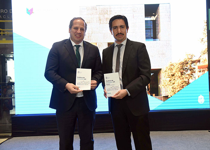 Fotografía del Vicerrector Académico UC, Fernando Purcell, junto al Subdirector de la Dirección de Inclusión, Pablo González, ambos sosteniendo una copia impresa de la actualización de la Política de Inclusión institucional