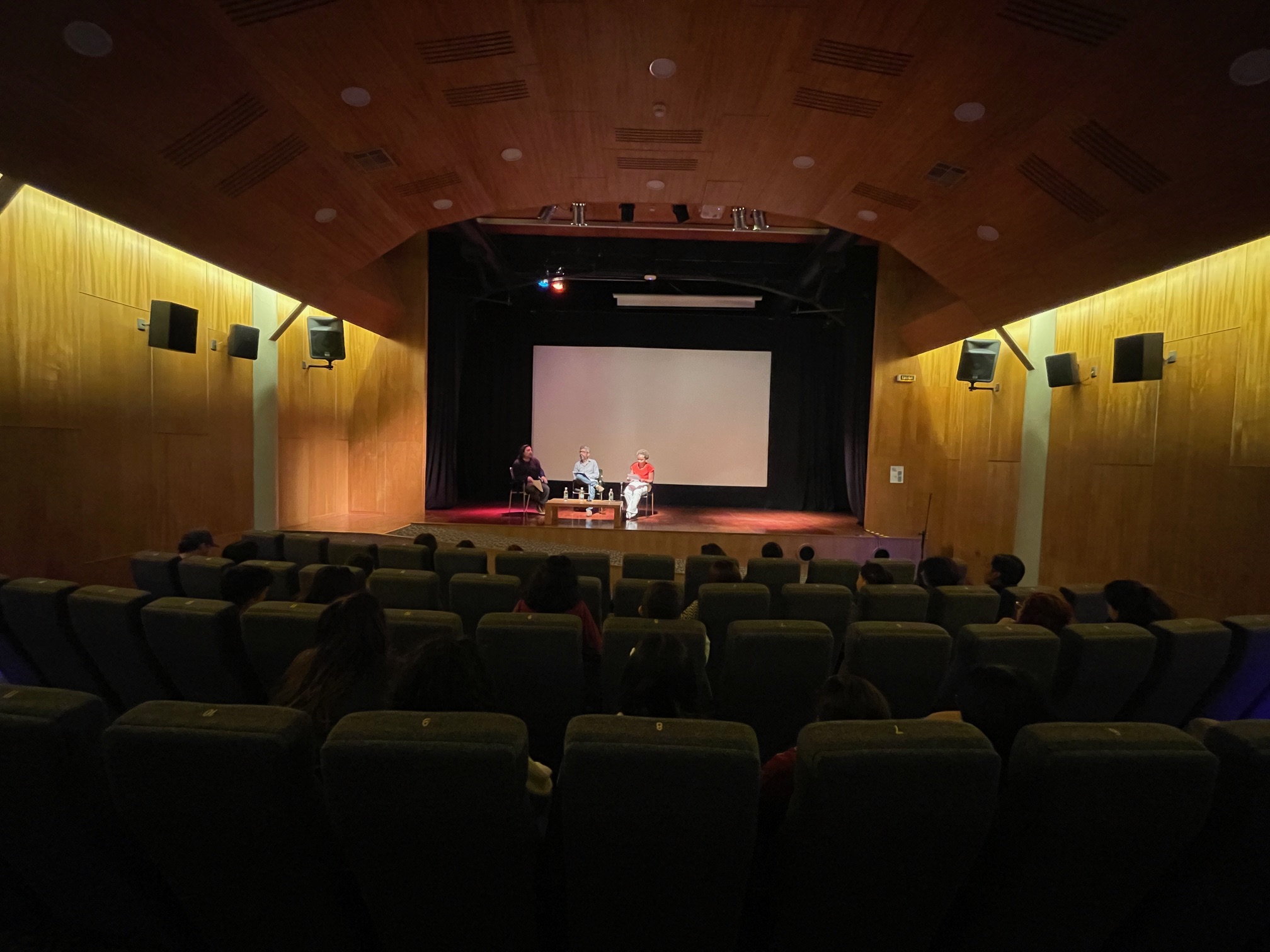 Fotografía del Cine UC enfocando al escenario central con panelistas de conversatorio al fondo 