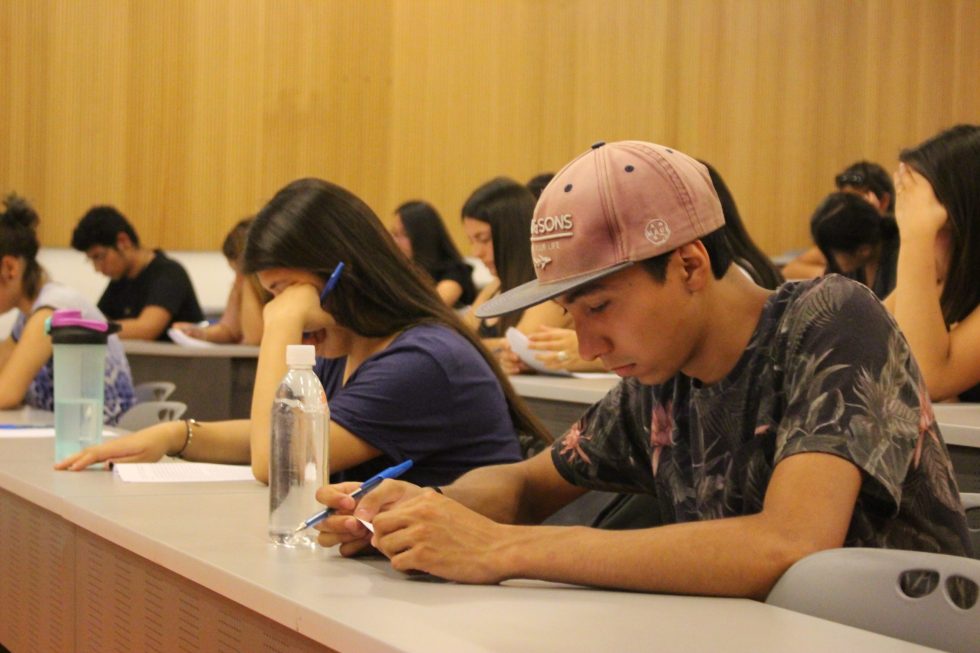 Estudiantes de primer año que ingresaron vía PACE UC rindiendo una prueba de diagnóstico de Lenguaje previo al ingreso en marzo en 2018 en una sala amplia, separados por un puesto.