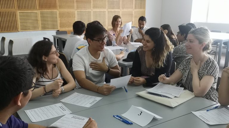 Grupo de estudiantes y profesionales, sentados en una mesa, conversando y sonriendo.