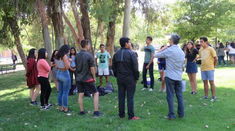 Estudiantes formando un círculo en explanada de pasto.