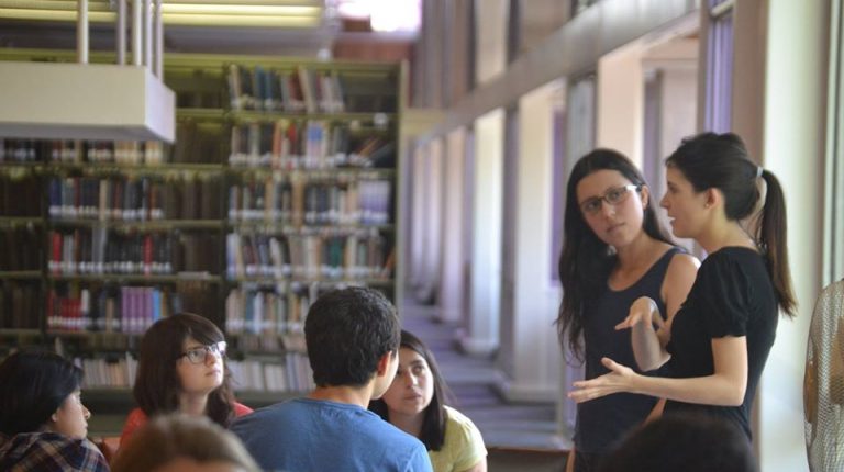Se encuentran estudiantes en una mesa de la Biblioteca San Joaquín UC, conversando con profesor.