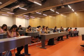 La imagen es tomada en una sala de clases de la UC, durante la aplicación de una prueba de diagnóstico y muestra a un grupo de estudiantes concentrados leyendo un documento que se encuentra sobre el escritorio.