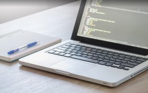 Computador portátil sobre mesa junto a un cuaderno y un lápiz.