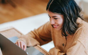 Joven mirando y sonriendo frente al computador.