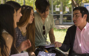 Alumnos y alumnas de la UC conversando con libros y cuadernos en sus manos.
