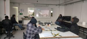 Estudiantes escolares de liceos PACE UC en actividad presencial en colegio, específicamente mirando el pizarrón donde se encuentra proyectada una película.