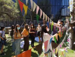 Estudiantes pegando post it con mensajes sobre hileras de banderines colgando, se encuentran al aire libre.
