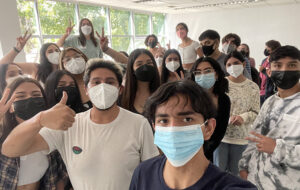Estudiantes y ayudantes de Inclusión saludando a la cámara con mascarilla en Jornada de Inserción vías de equidad 2022