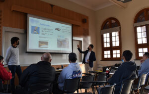 Profesional de la Dirección de Inclusión hablando en capacitación indicando elementos de una presentación PPT proyectada en un telón