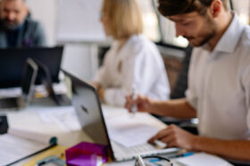 Fotografía de personas en mesa de trabajo con computadores y materiales de oficina.