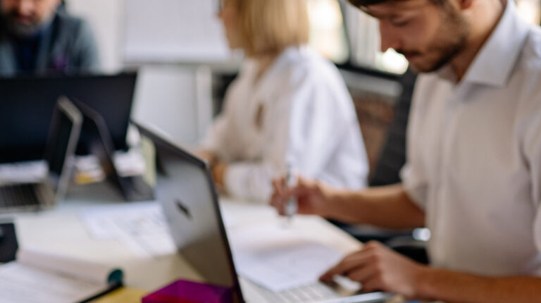 Fotografía de personas en mesa de trabajo con computadores y materiales de oficina.