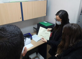 Fotografía de personas adultas en una sala tocando y mirando un papel con impresión en Braille.