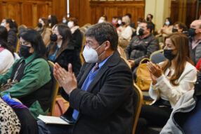 Fotografía de personas sentadas aplaudiendo en un salón, llevan mascarilla puesta