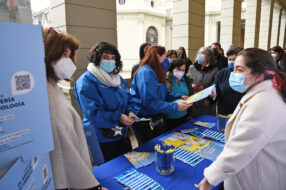 Fotografía de un mesón de Admisión UC con folletería, dos estudiantes conversando con docentes de colegio