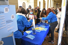 Fotografía de un mesón de Admisión UC con folletería, dos estudiantes conversando con docentes de colegio