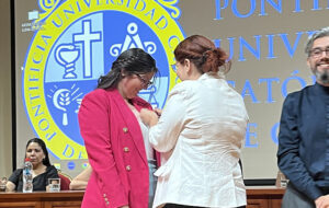 Fotografía de dos personas una poniéndole un broche en la chaqueta a la otra