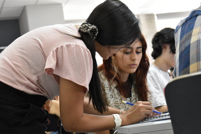 Fotografía de una estudiante señalando a otra en su cuaderno