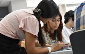Fotografía de una estudiante señalando a otra en su cuaderno