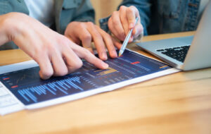 Fotografía de las manos de dos personas, señalando datos en un documento, una de ellas con un lápiz