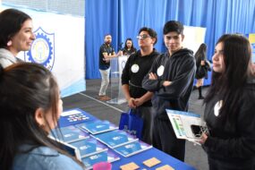 Estudiantes secundarios realizando preguntas a profesionales PACE UC en stand de Feria Vocacional