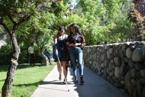 Profesionales UC realizando ejercicio práctico sobre cómo asistir a persona con discapacidad visual por el Campus San Joaquín