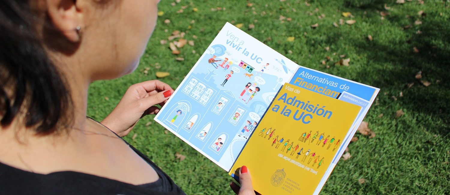 Joven mujer sostiene un folleto con la información de las vías de admisión que tiene la Universidad Católica y folleto con Alternativas de Financiamiento de la misma institución.