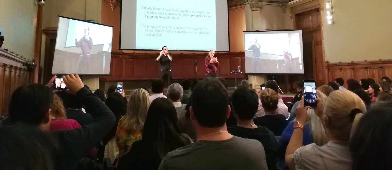 Paddy Ladd, parado en escenario junto a su intérprete oyente de Lengua de Señas de Inglaterra, en el contexto del seminario “Construyendo puentes para la educación de personas sordas”.