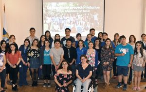 Funcionarios de PIANE UC y la Dirección de Asuntos Estudiantiles DAE, dispuestos en tres filas junto a estudiantes que pertenecen al equipo de Pares Educadores de Salud PES. A la izquierda, se visualizan las banderas de Chile y la Universidad Católica en mástiles.