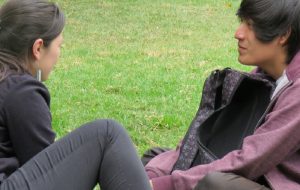 Tutora de PACE UC en sesión de apoyo con estudiante del programa, sentados en explanada de pasto en Campus San Joaquín.