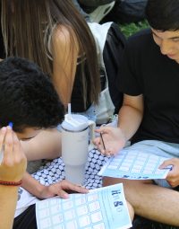 Dos estudiantes de PACE UC Educación Superior sentados en el pasto y jugando al bingo