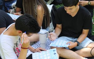 Dos estudiantes de PACE UC Educación Superior sentados en el pasto y jugando al bingo
