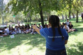 Ayudante Operativa PACE UC de espaldas, entregando información a grupo de estudiantes sentados en el pasto